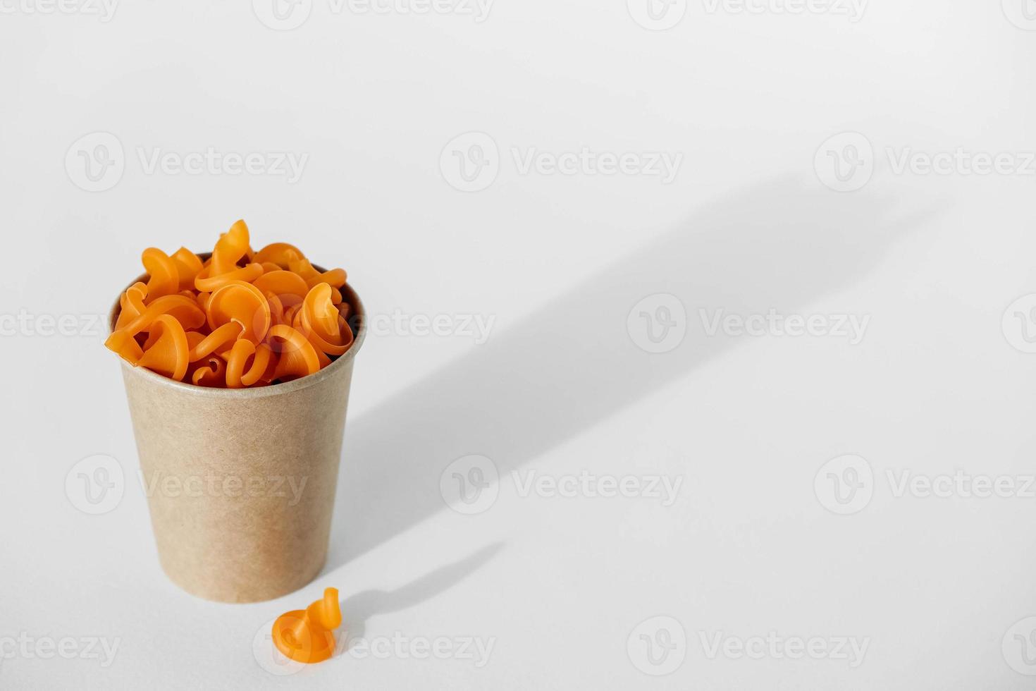 Orange pasta in a disposable kraft paper cup on a white background. Copy, empty space for text photo