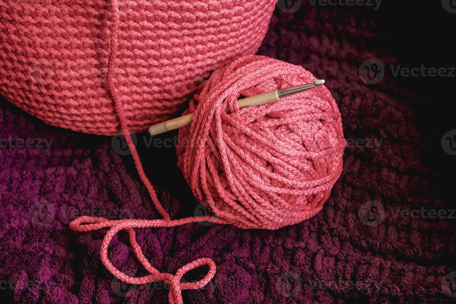 Ball of pink thread with a needle and knitted fabric on a background of purple material. Copy, empty space for text photo