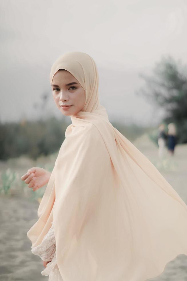 Beautiful islamic female model wearing hijab fashion, a modern wedding dress for muslim woman walks along the sand and the sea. A asian girl model using hijab having fun at the beach. Photo prewedding