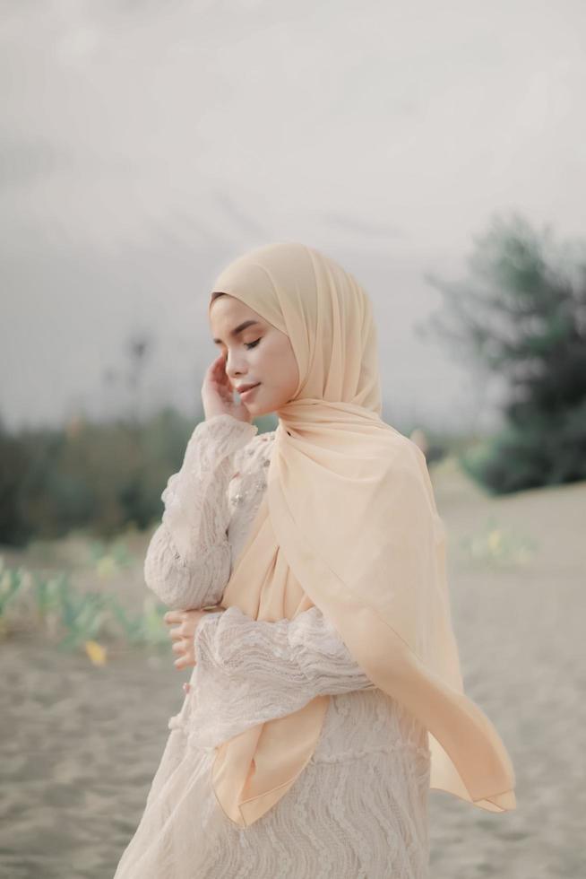 Beautiful islamic female model wearing hijab fashion, a modern wedding dress for muslim woman walks along the sand and the sea. A asian girl model using hijab having fun at the beach. Photo prewedding