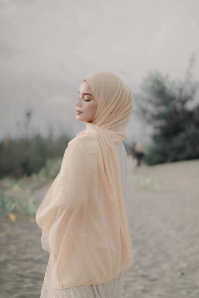 Beautiful islamic female model wearing hijab fashion, a modern wedding dress for muslim woman walks along the sand and the sea. A asian girl model using hijab having fun at the beach. Photo prewedding