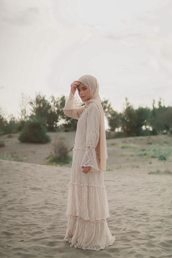 hermosa modelo femenina islámica con moda hijab, un vestido de novia moderno para mujeres musulmanas camina por la arena y el mar. una modelo asiática usando hijab divirtiéndose en la playa. foto preboda