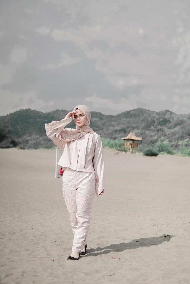 Beautiful islamic female model wearing hijab fashion, a modern wedding dress for muslim woman walks along the sand and the sea. A asian girl model using hijab having fun at the beach. Photo prewedding