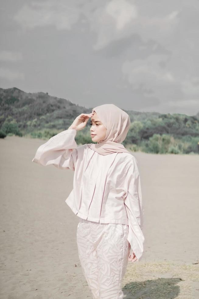 Beautiful islamic female model wearing hijab fashion, a modern wedding dress for muslim woman walks along the sand and the sea. A asian girl model using hijab having fun at the beach. Photo prewedding