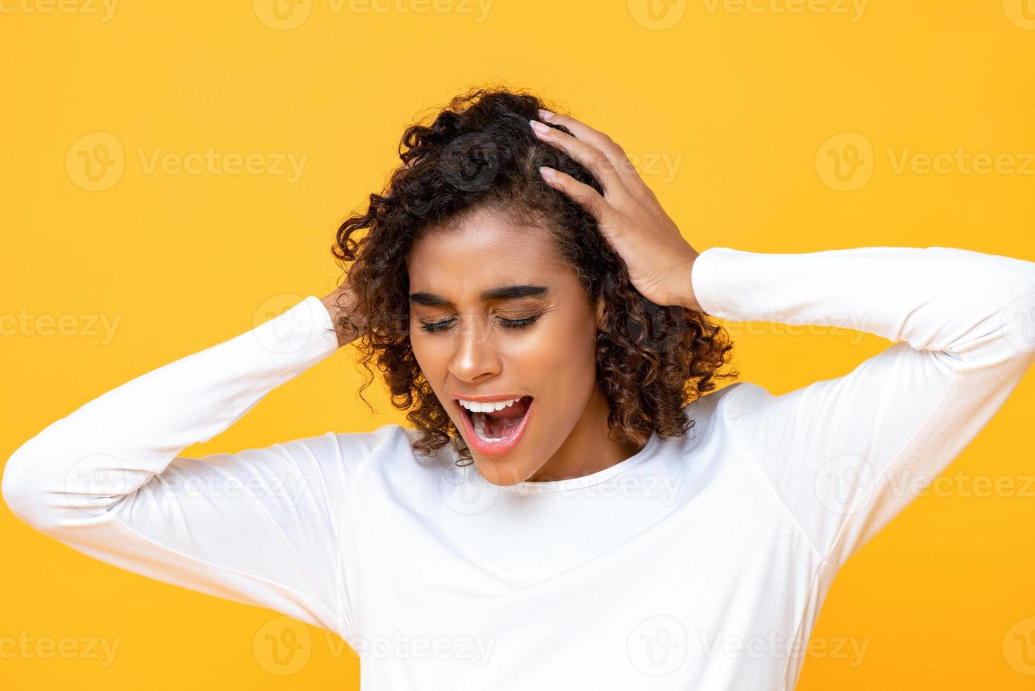 retrato cerrado de una mujer afroamericana confundida gritando mientras sostenía su cabeza con ambas manos en un estudio aislado de fondo amarillo foto