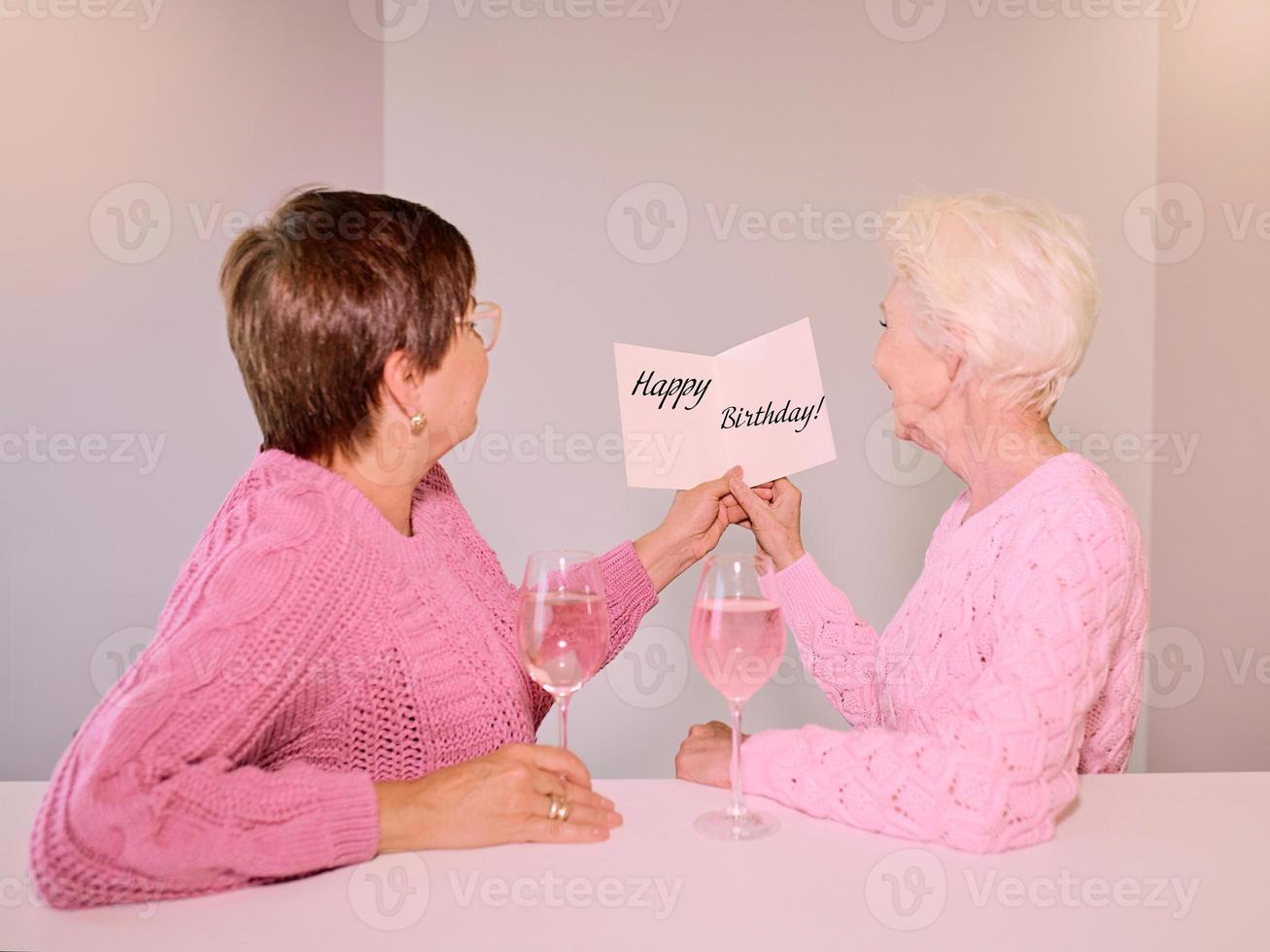 Two mature women drinking wine and giving a post card picture