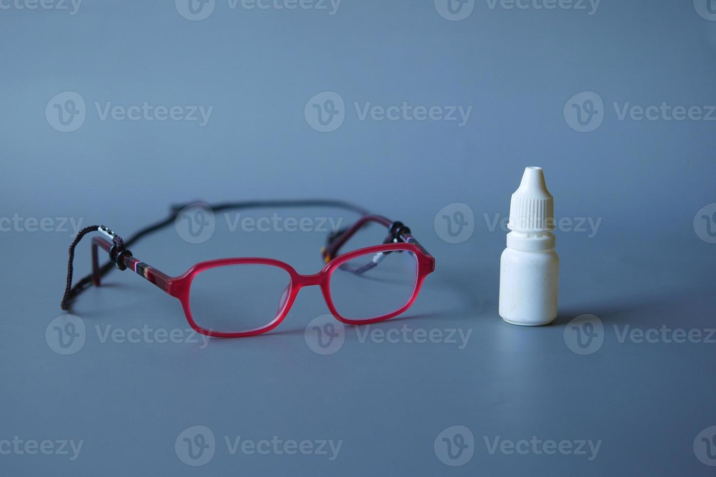 close up of eye drop bottle and eyeglass on black photo