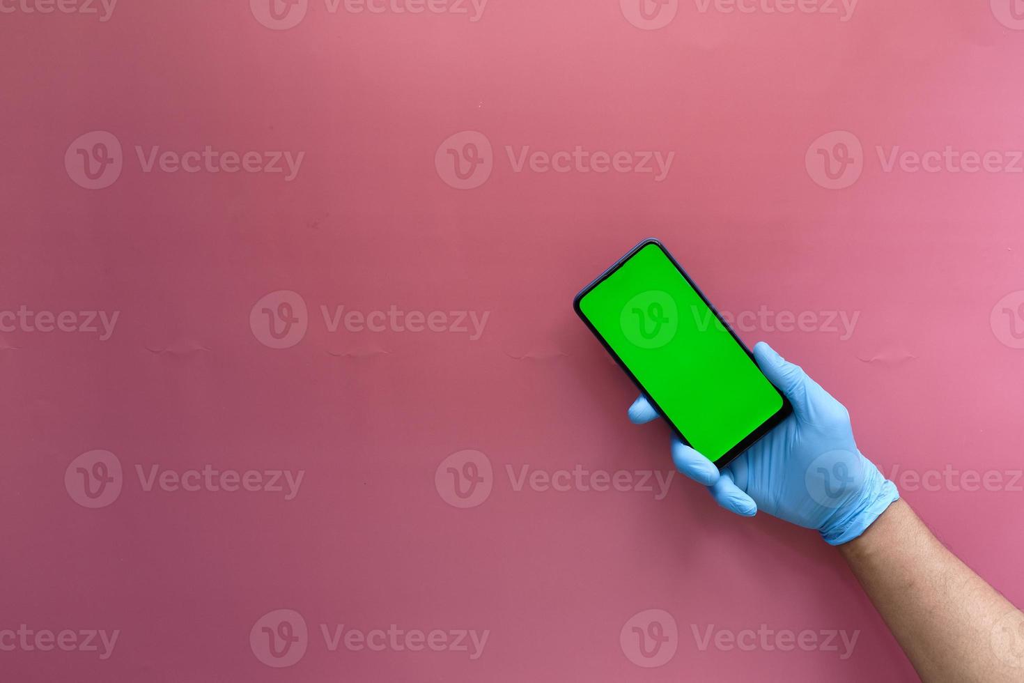 hand in latex gloves holding smart phone with green screen photo