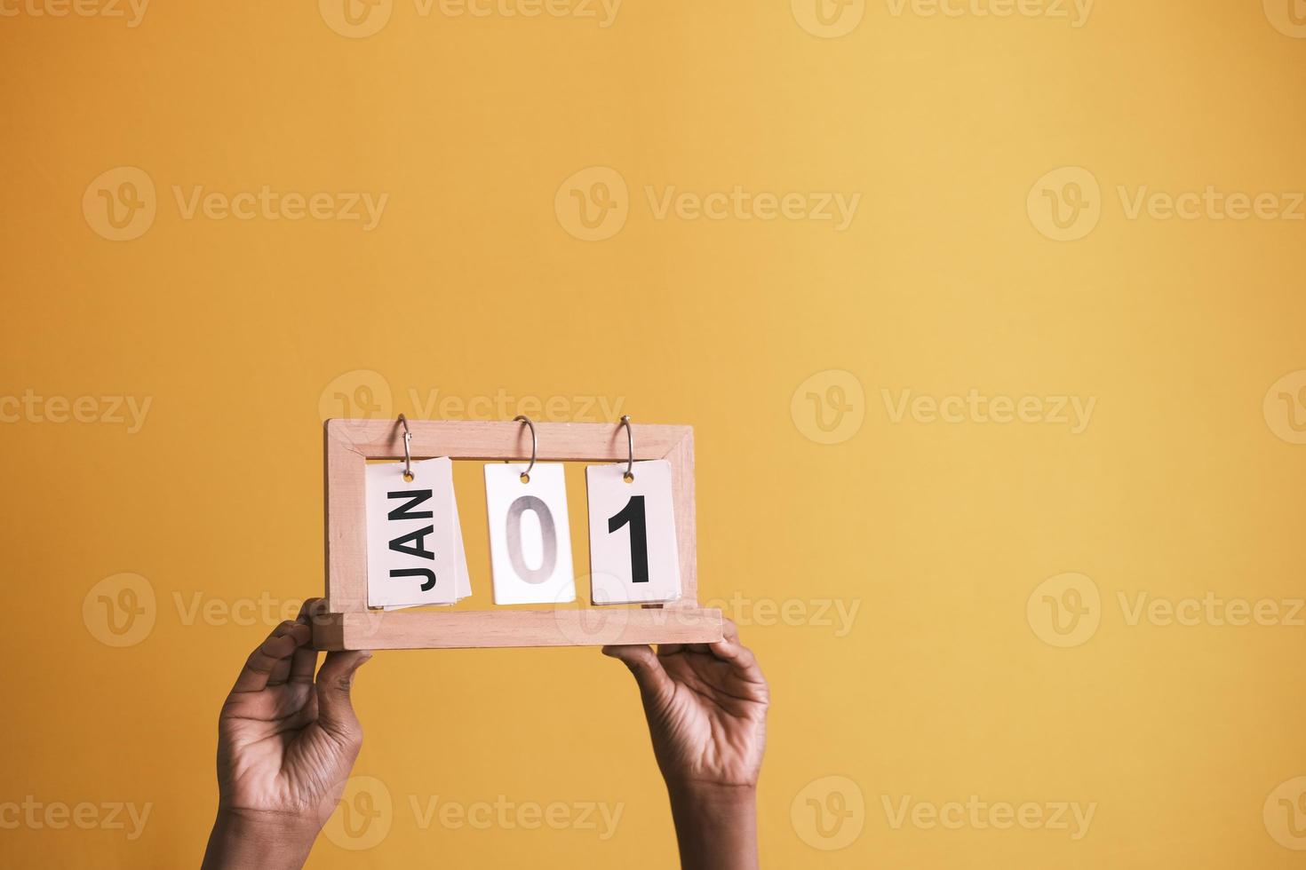 sosteniendo el calendario de madera fijado el 1 de enero contra el fondo amarillo foto