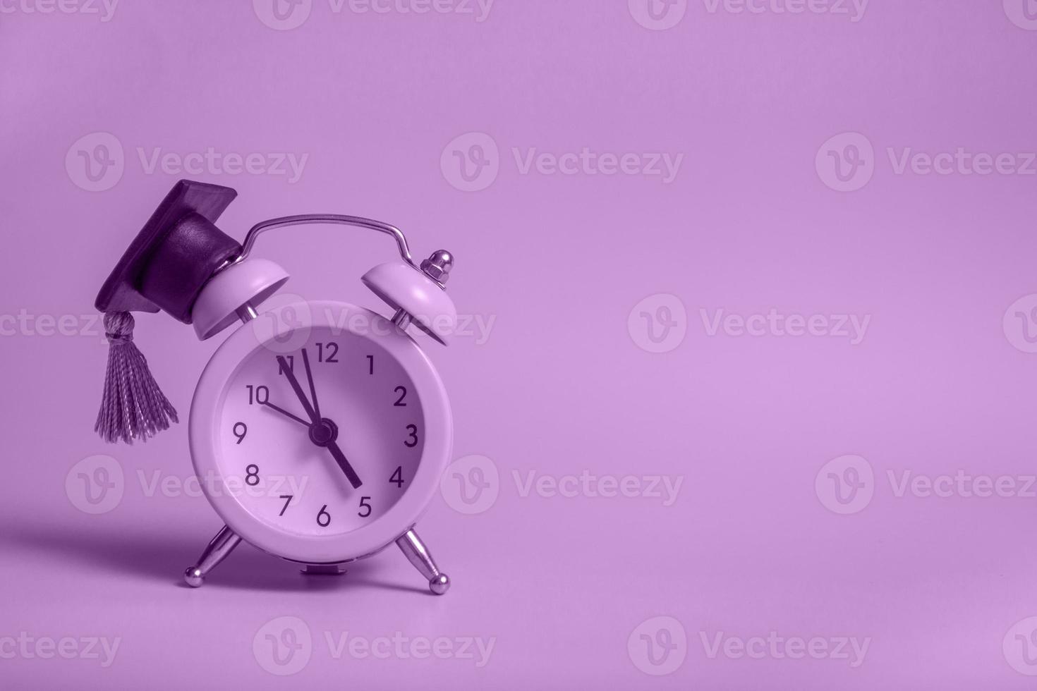Despertador amarillo con gorra de graduación sobre fondo violeta primer plano con espacio de copia foto