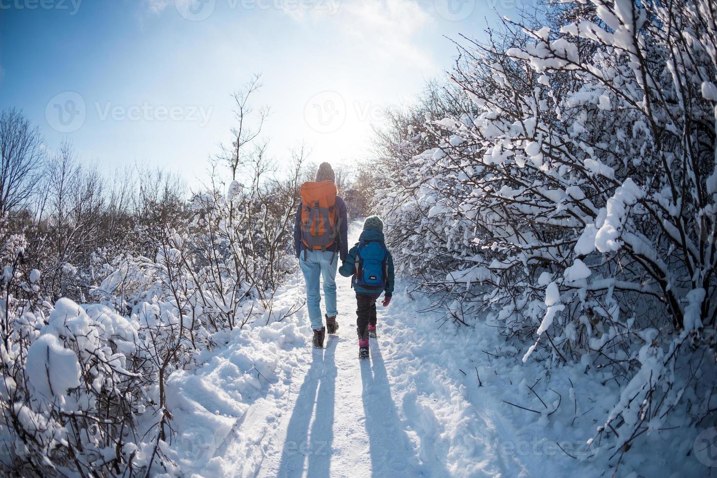 A child with a backpack walks with mother in a snowy forest photo