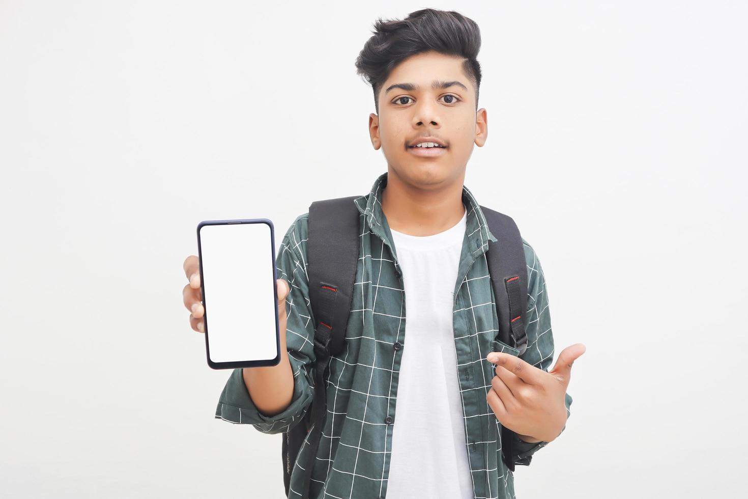 joven estudiante universitario indio que muestra la pantalla del teléfono inteligente con fondo blanco. foto