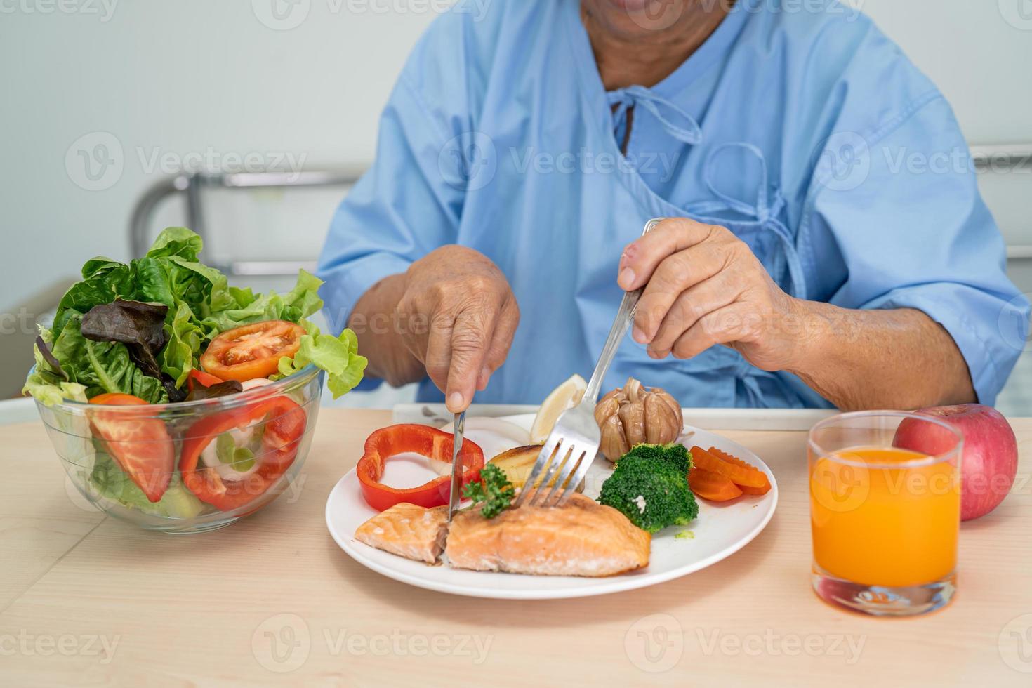 Asian senior or elderly old lady woman patient eating Salmon steak breakfast with vegetable healthy food while sitting and hungry on bed in hospital. photo