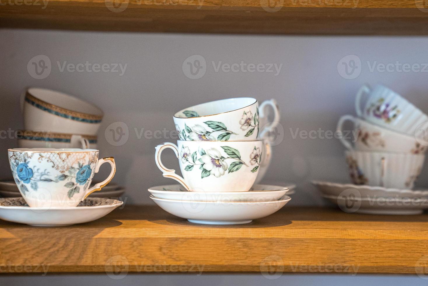 Assortment of floral pattern tea cups with saucers on shelves photo