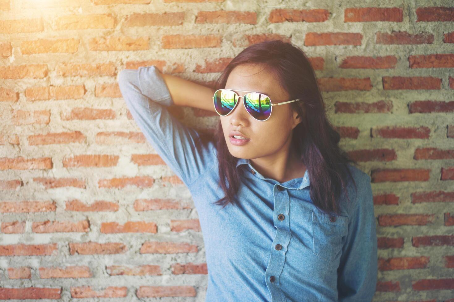 Portrait of a beautiful smiling hipster wearing sunglasses against a red brick wall. photo