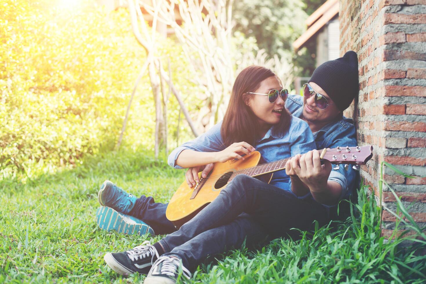 el hombre hipster le enseña a tocar la guitarra a su novia mientras se sienta en la hierba y se ve tan feliz. pareja en concepto de amor. foto