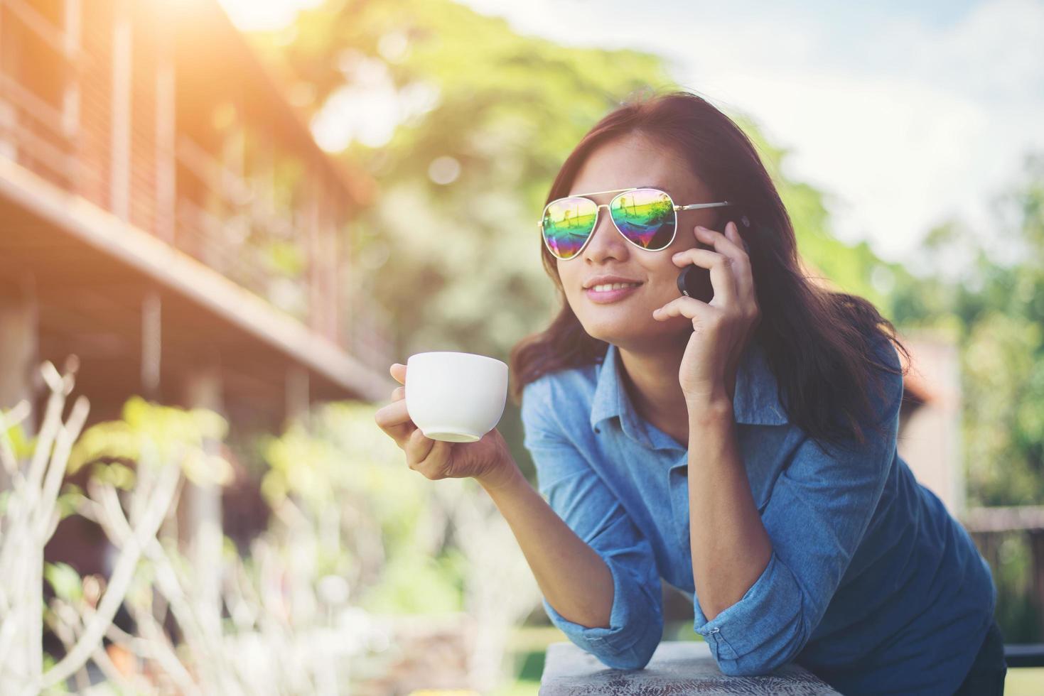 joven hipster hablando por teléfono mientras sostiene una taza de café por la mañana y sonríe. relajante concepto de vacaciones. foto