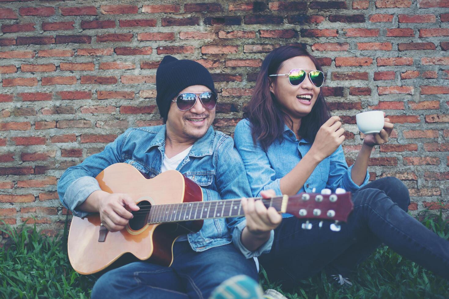 hombre hipster tocando la guitarra para su novia al aire libre contra la pared de ladrillo, disfrutando juntos. foto