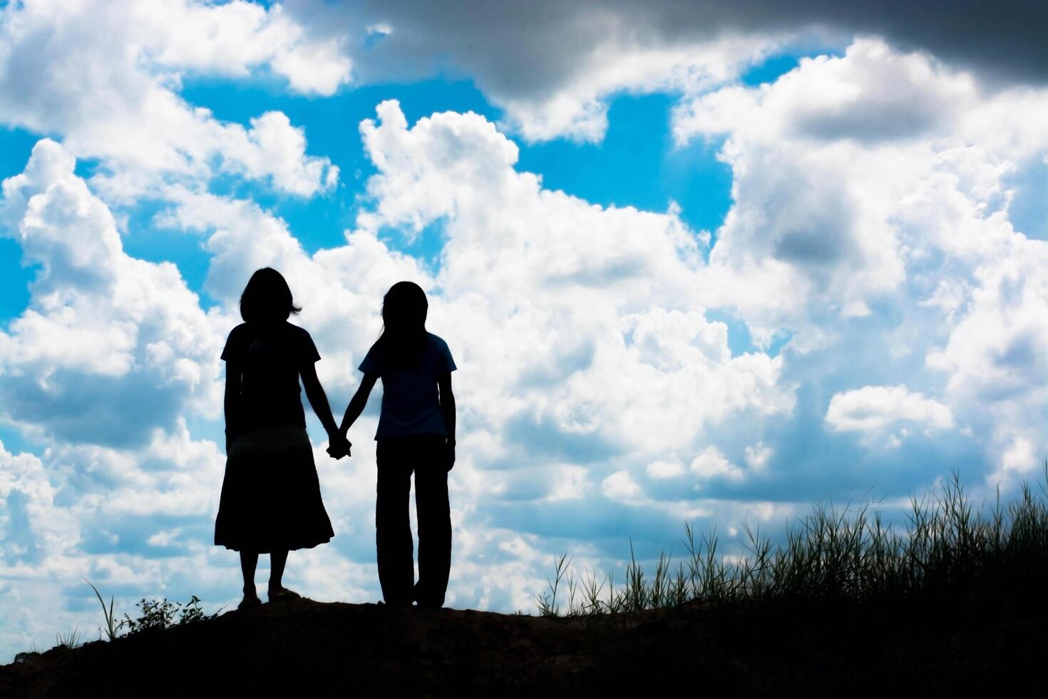 silhouette of two girls facing each other hold hands together photo