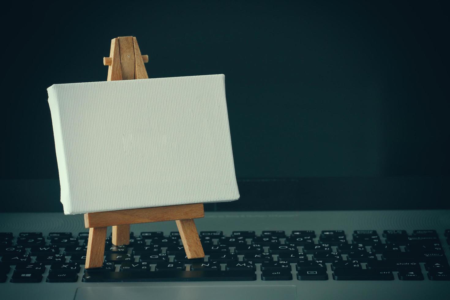 blank canvas and wooden easel on laptop computer as concept photo