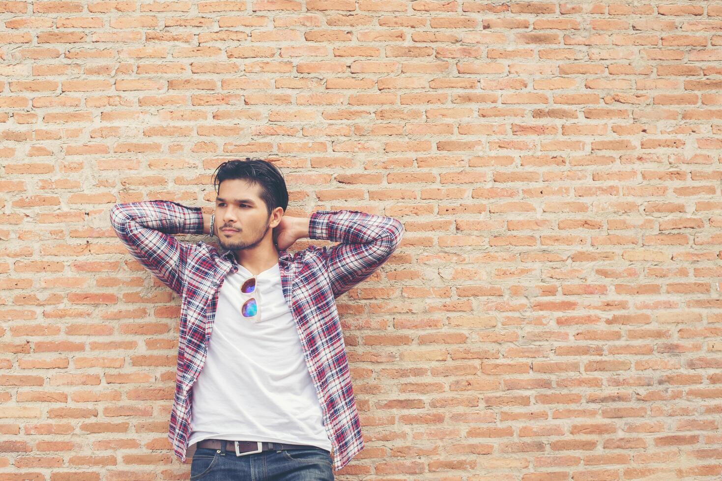 Young handsome hipster man wearing plaid shirt and jeans against a brick wall. photo