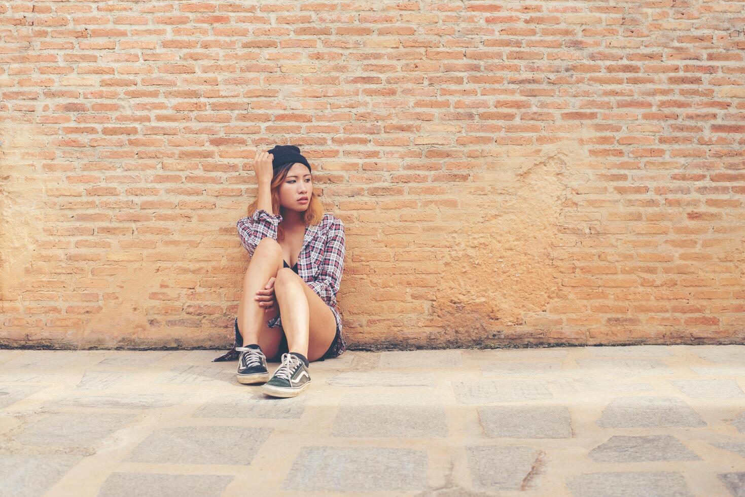 mujer joven triste sentada sola contra la pared de ladrillo. foto