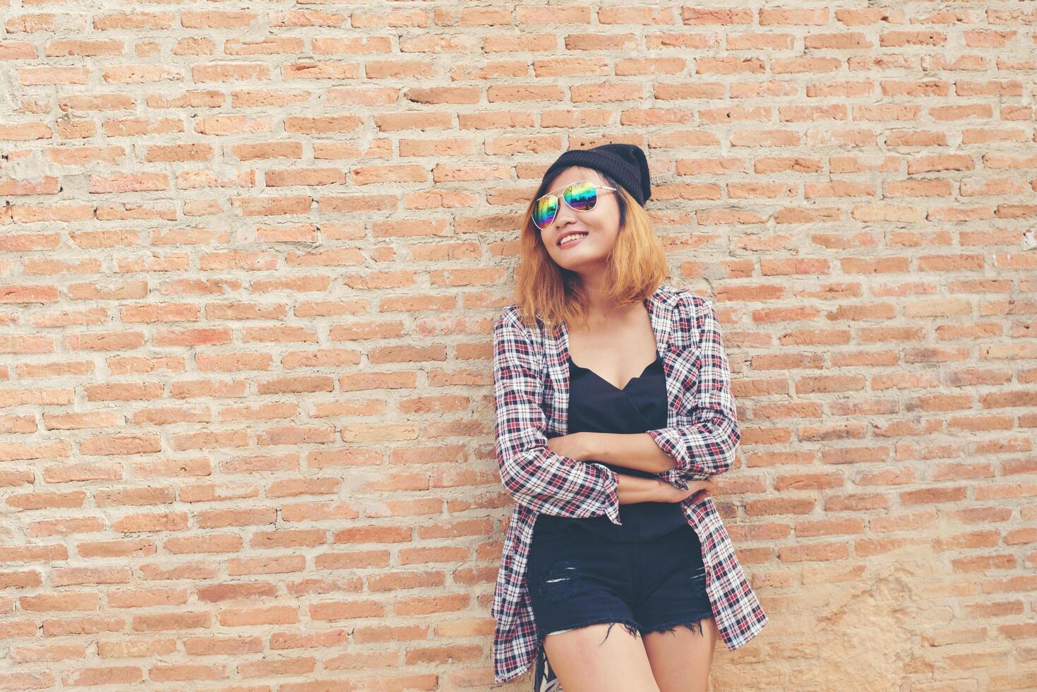 Young pretty hipster woman standing against brick wall posing smiling enjoy with nice time. photo