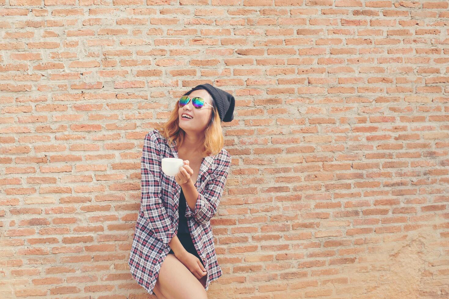 Cheerful woman in the street drinking morning coffee against brick wall. photo