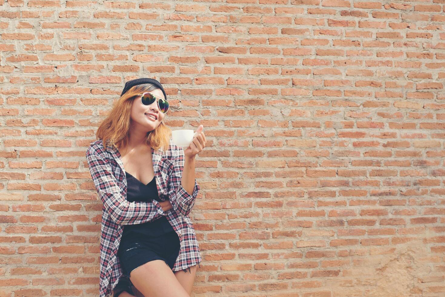 Cheerful woman in the street drinking morning coffee against brick wall. photo