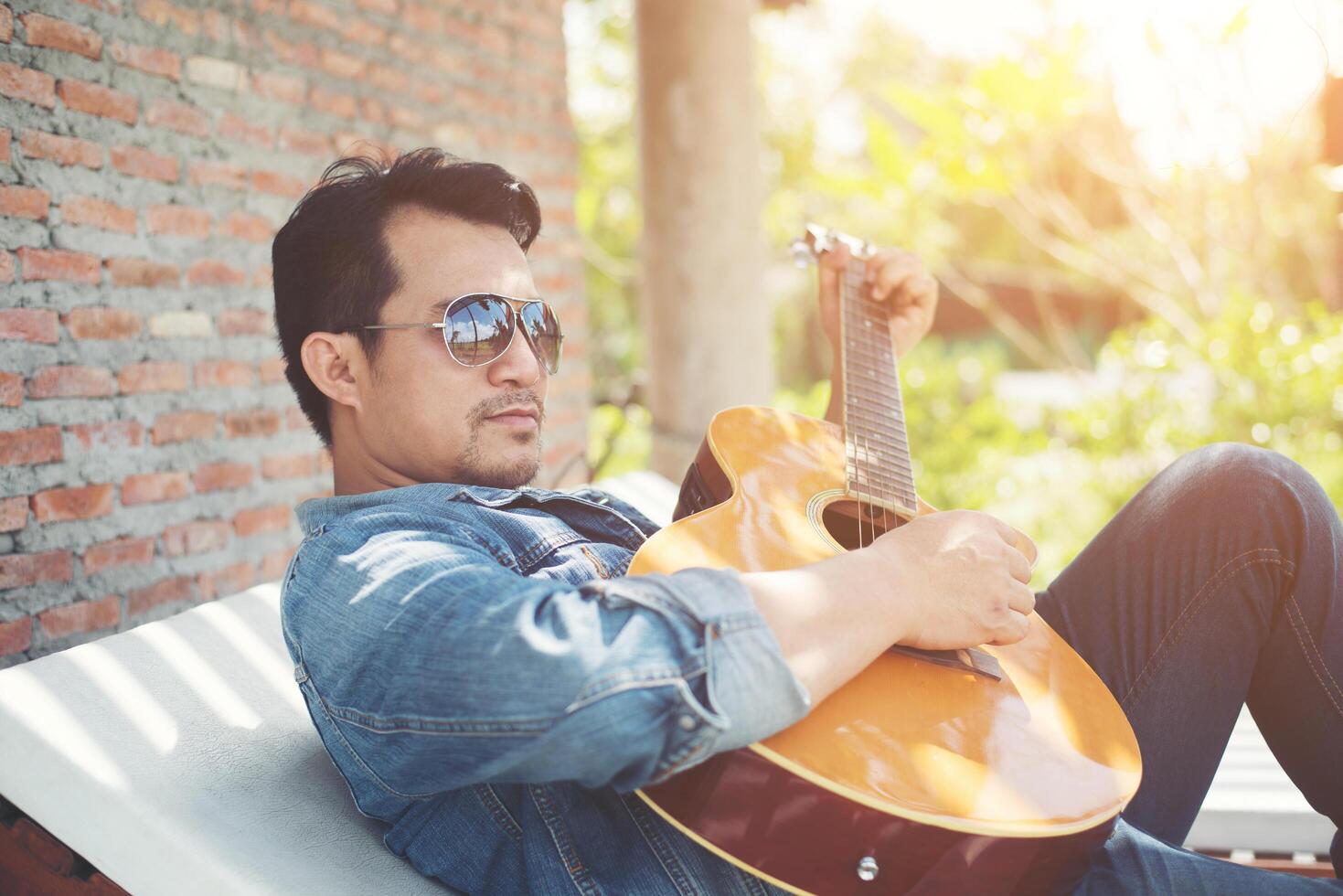 hombres hipster guapos practican para tocar la guitarra mientras él disfruta de la relajación con la naturaleza alrededor. foto