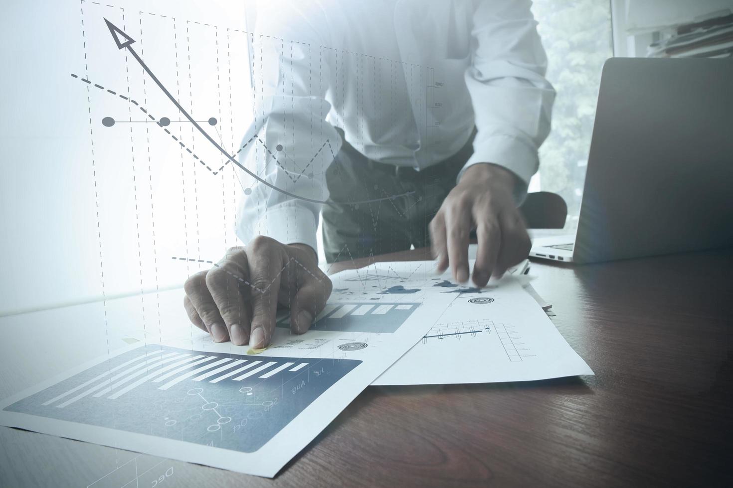 close up of business man hand working on laptop computer with business graph information diagram on wooden desk as concept photo