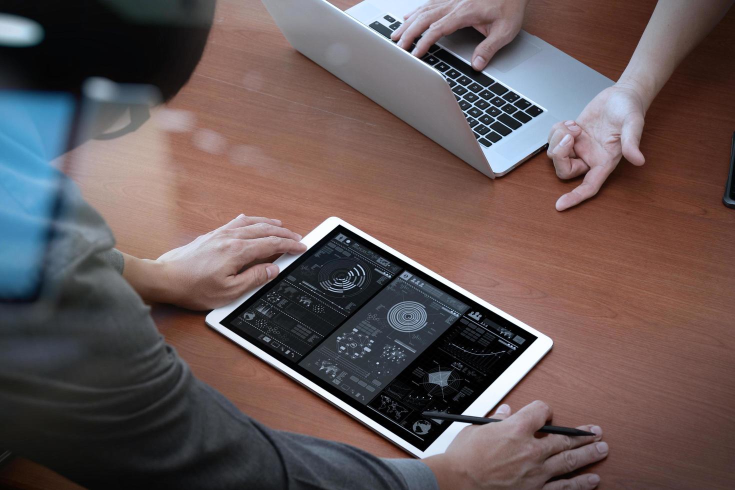 top view of two colleagues discussing data with new modern computer laptop and pro digital tablet with digital business strategy layer effect on wooden desk as concept photo