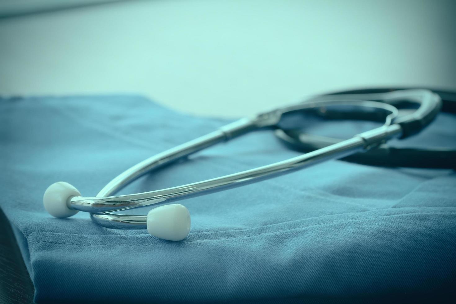 estetoscopio con bata azul de médico sobre una mesa de madera con dof superficial uniformemente emparejado y fondo foto