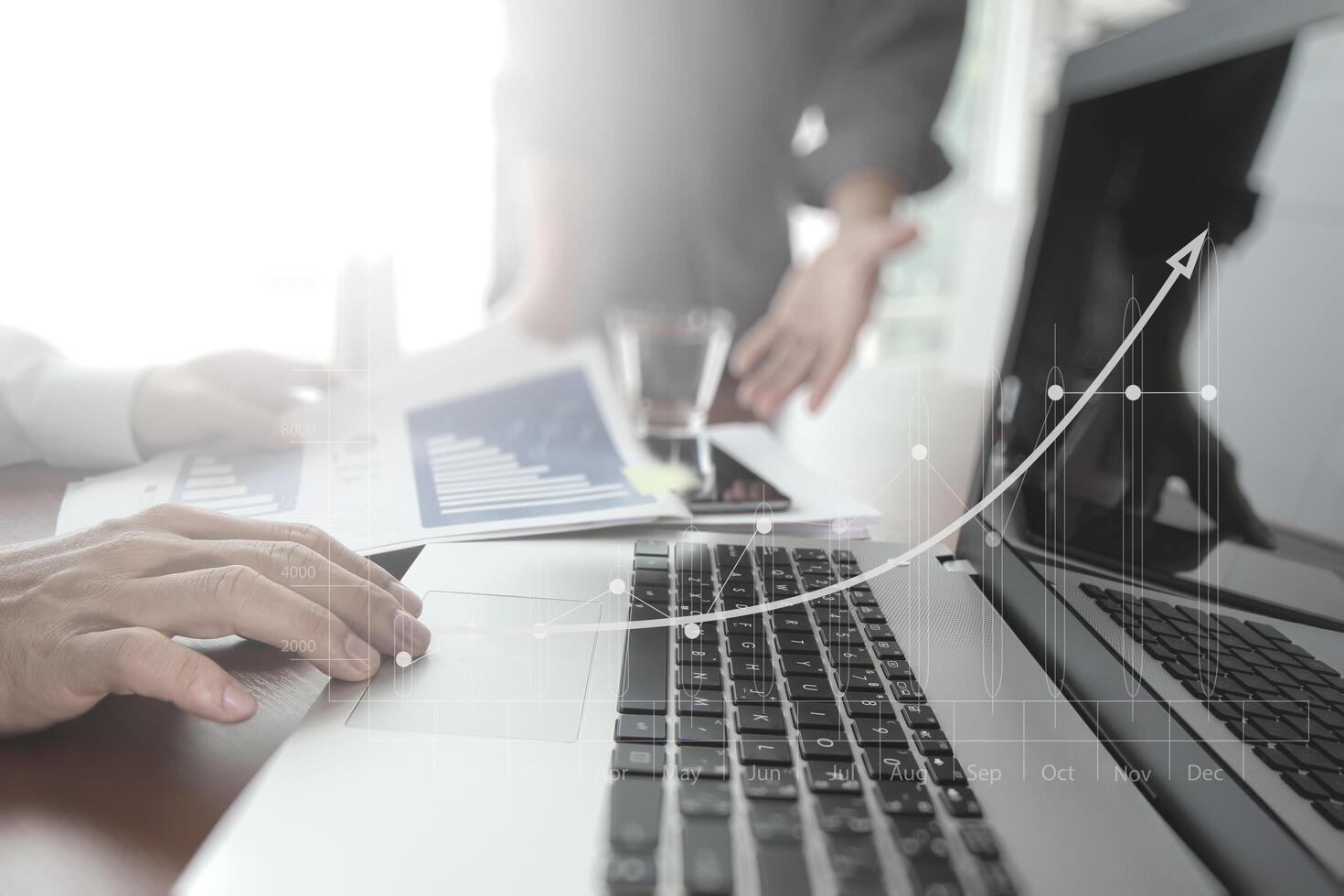 business documents on office table with smart phone and digital tablet and laptop computer and two colleagues discussing data in the background photo