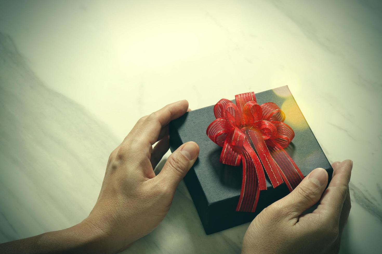 entrega de regalos, mano de hombre sosteniendo una caja de regalo en un gesto de dar sobre fondo de mesa de mármol gris blanco, vintage foto