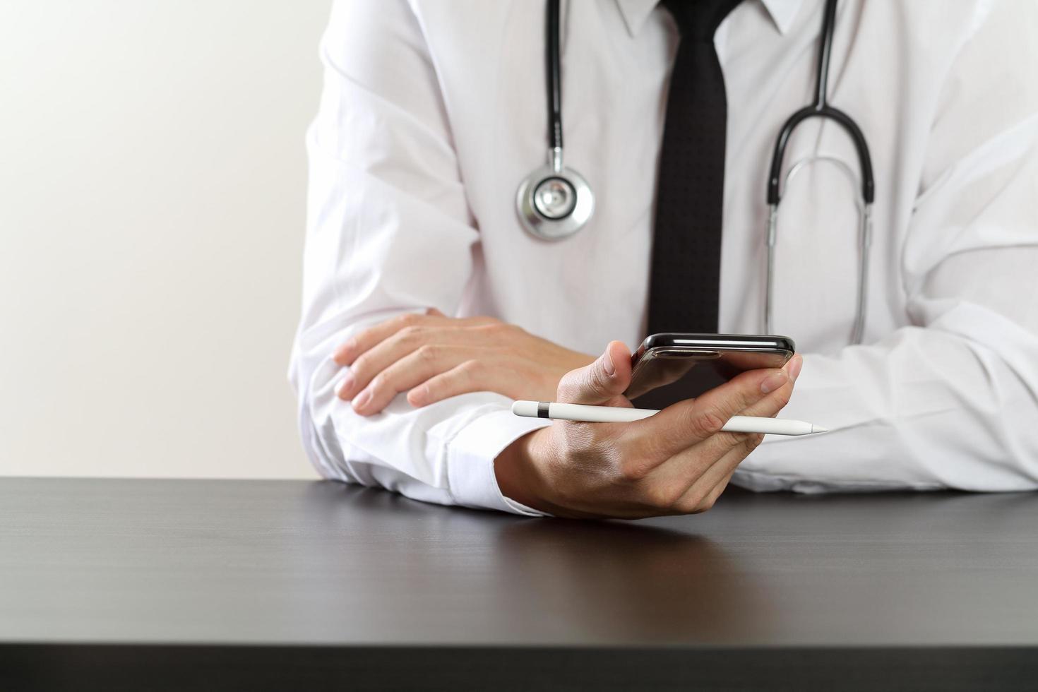 close up of smart medical doctor working with smart phone and stethoscope on dark wooden desk photo