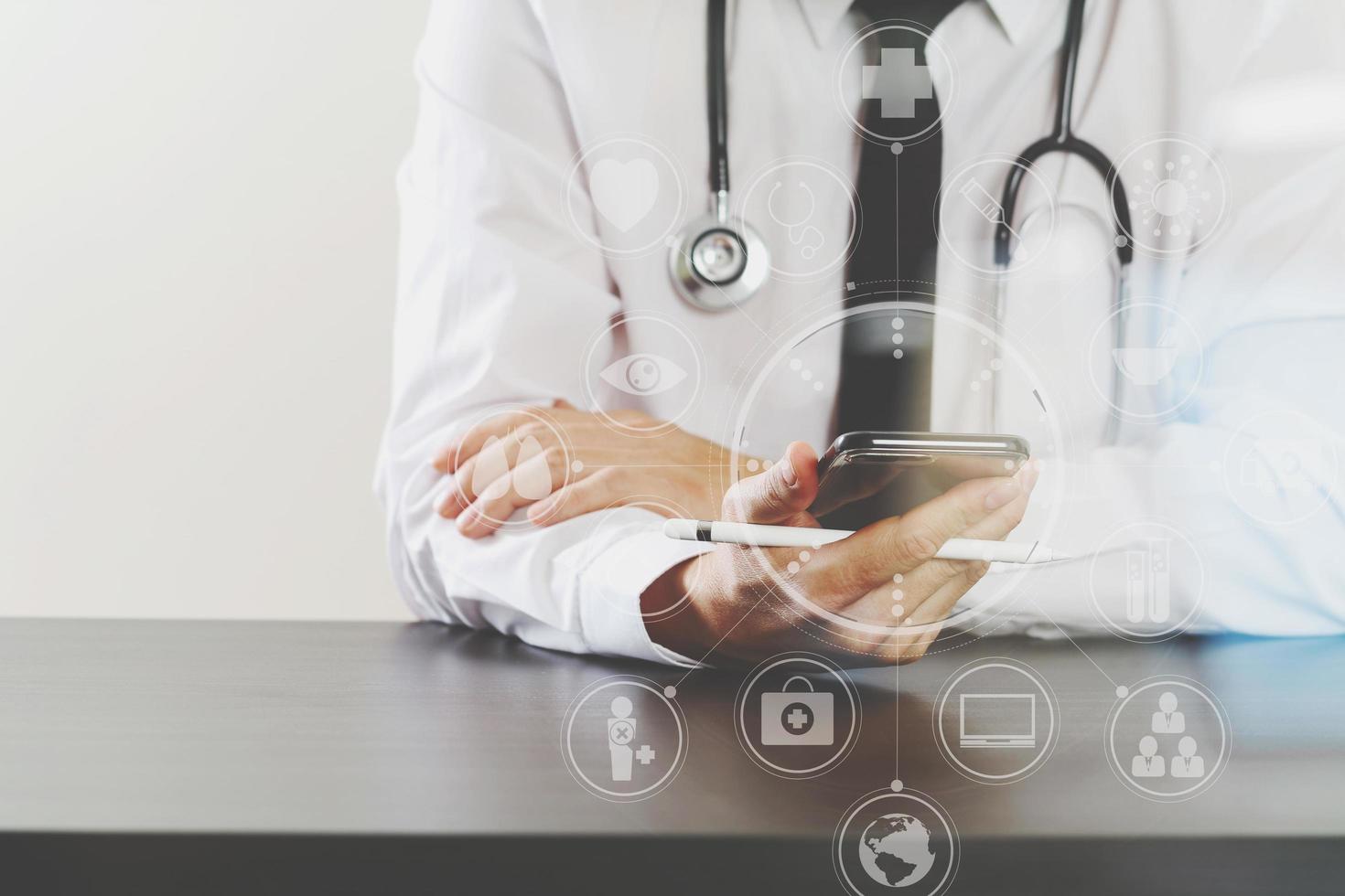 close up of smart medical doctor working with smart phone and stethoscope on dark wooden desk with virtual icon diagram photo
