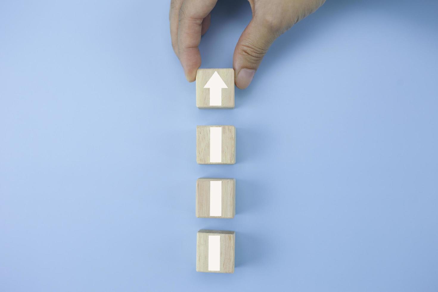 Closeup man hand arranging wood cube stacking as step stair with arrow up symbol photo