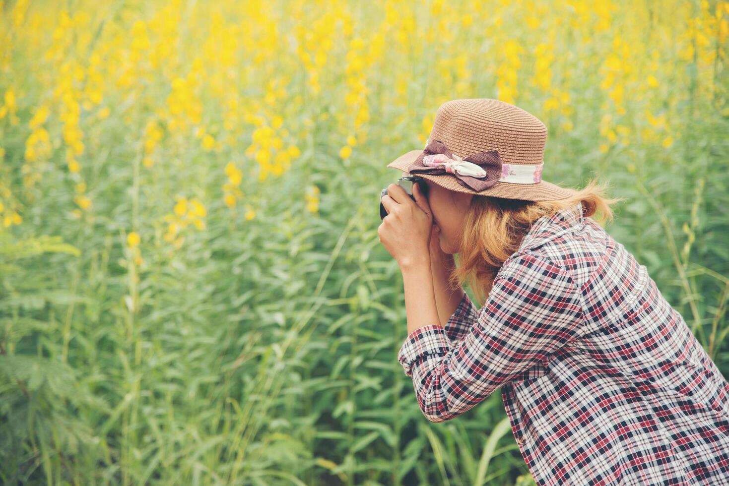 Happy woman in yellow flower field hloding with retro camera outdoors,enjoying nature. photo