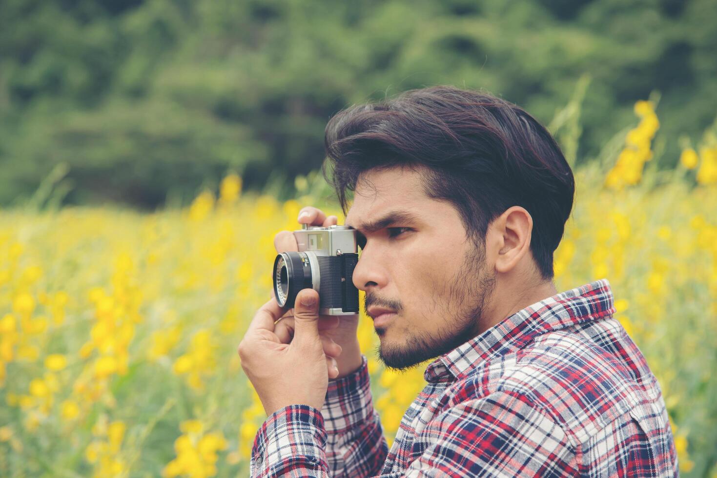 Young handsome hipster man photographing with retro camera with nature yellow flower field. photo