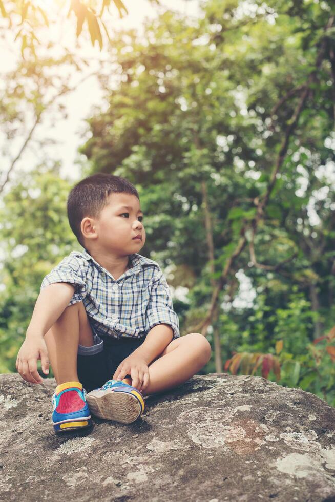 Sad little boy sitting on rock, in park. photo