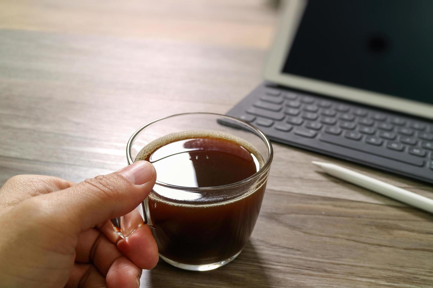 mano sujetando una taza de café o té y un teclado inteligente con base de mesa digital, lápiz óptico sobre una mesa de madera, efecto de filtro foto