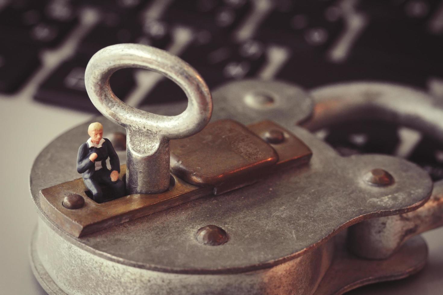 Internet security concept-miniature businessman stand on old key and padlock on laptop computer keyboard photo