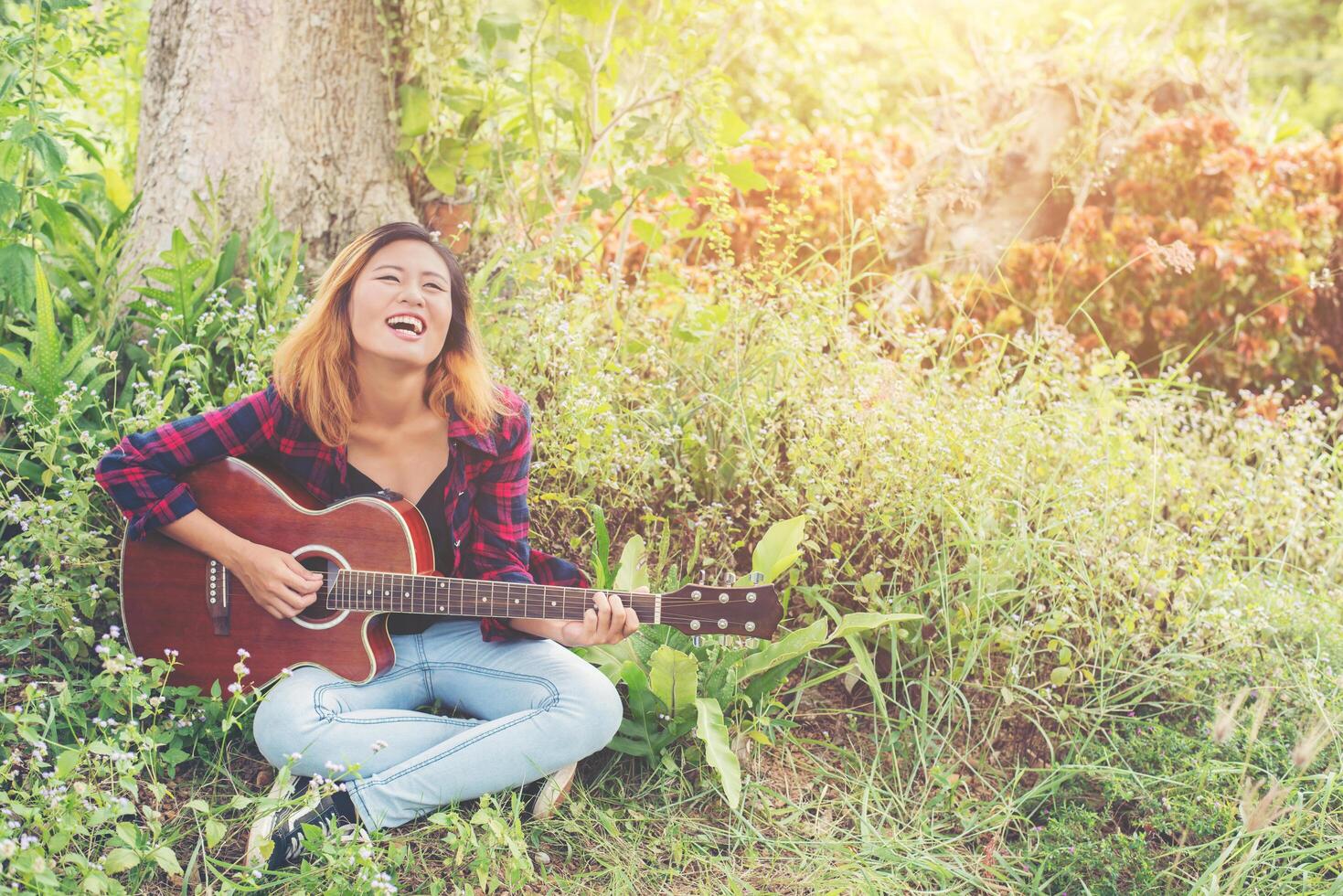 Young beautiful hipster woman playing guitar sitting on grass in the park, Relaxing with nature. photo