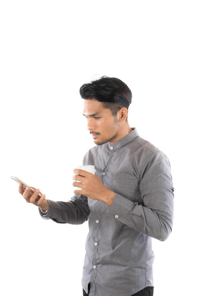 joven hipster mirando su teléfono inteligente mientras la taza de café en las manos está aislada en el fondo blanco. foto