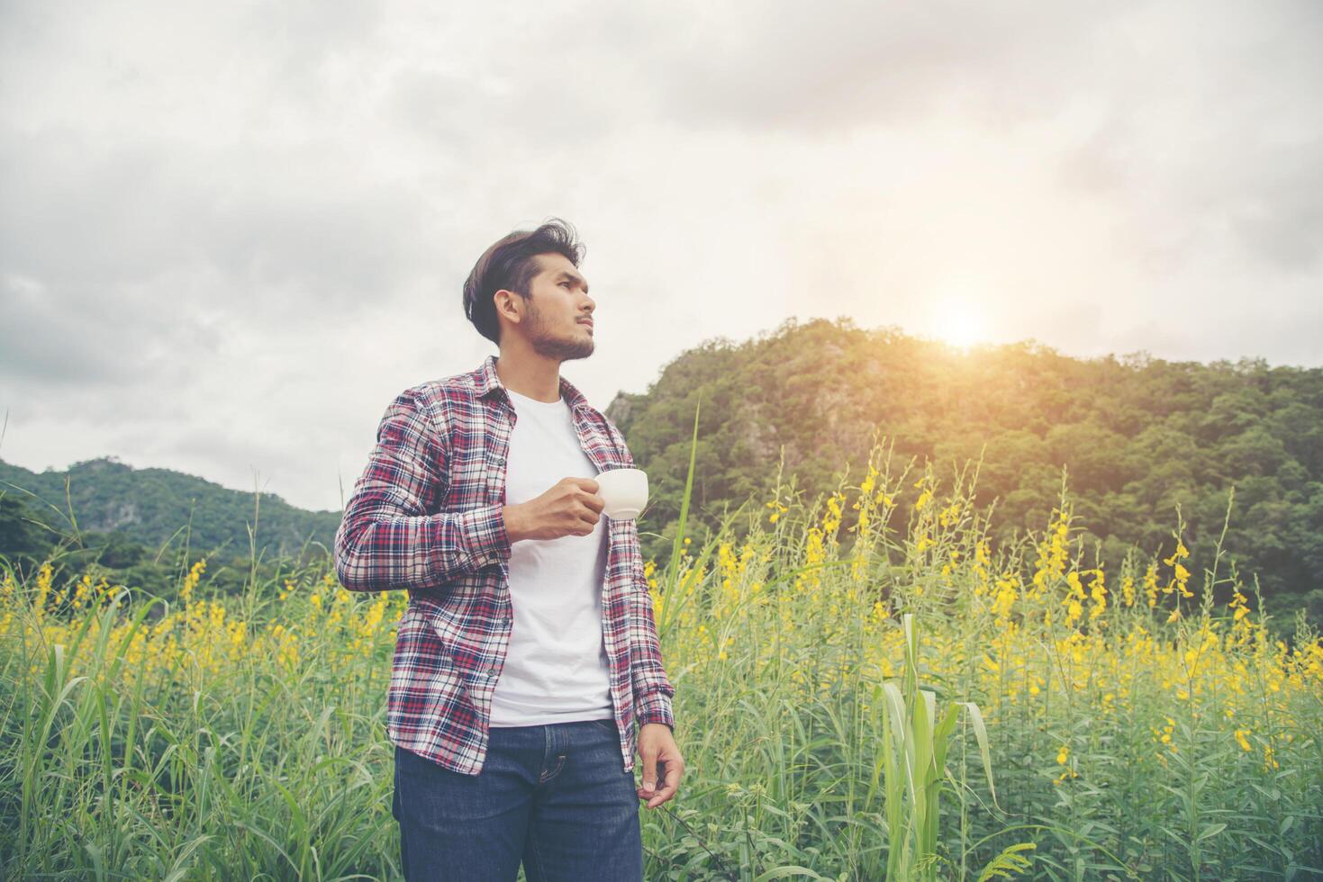 Bearded man with cup of morning coffee walking in the flower field. photo