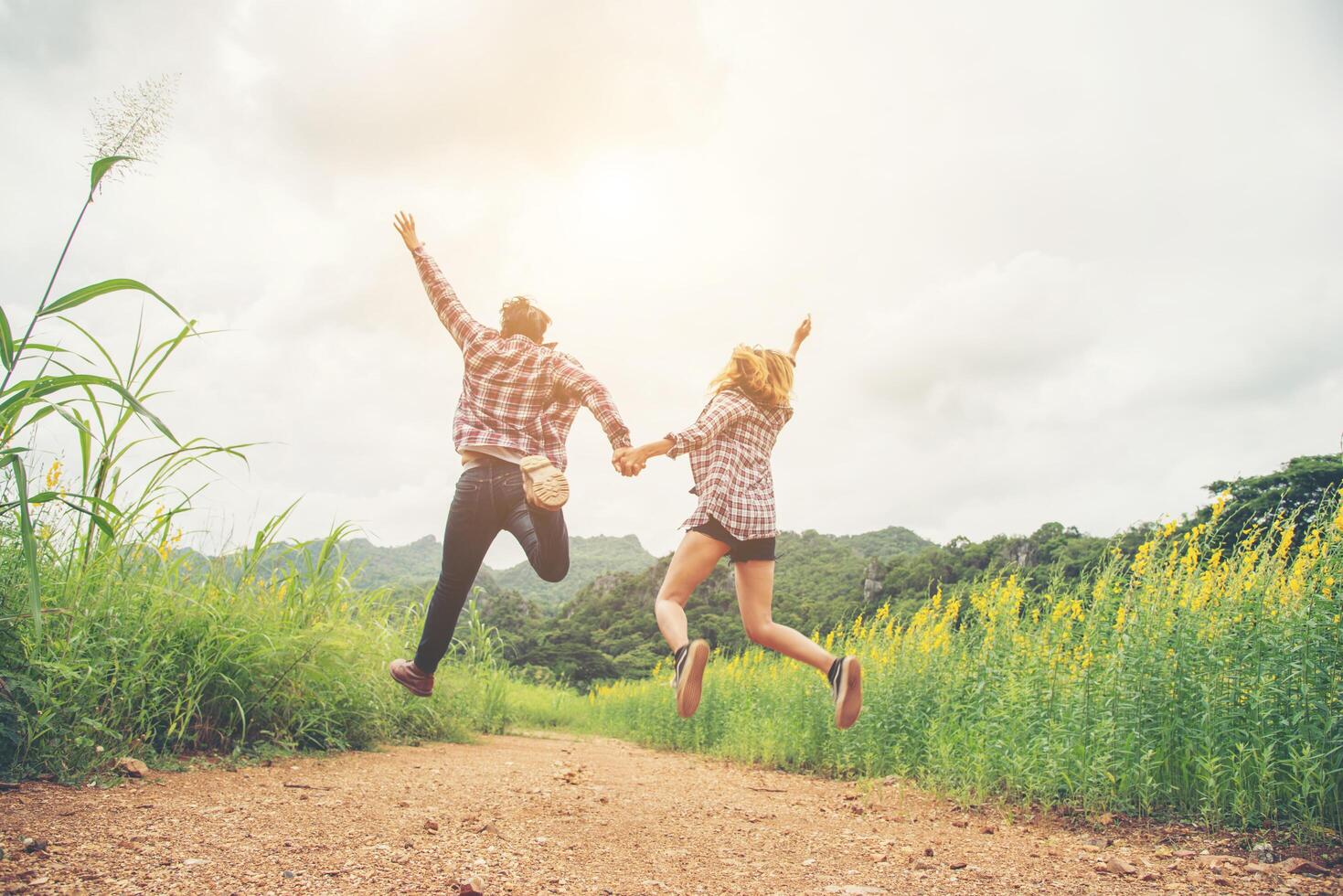 Young hipster couple in love outdoor jumping at yellow flower field with mountain sunset background. Jump up high enjoying freedom and enjoy. photo