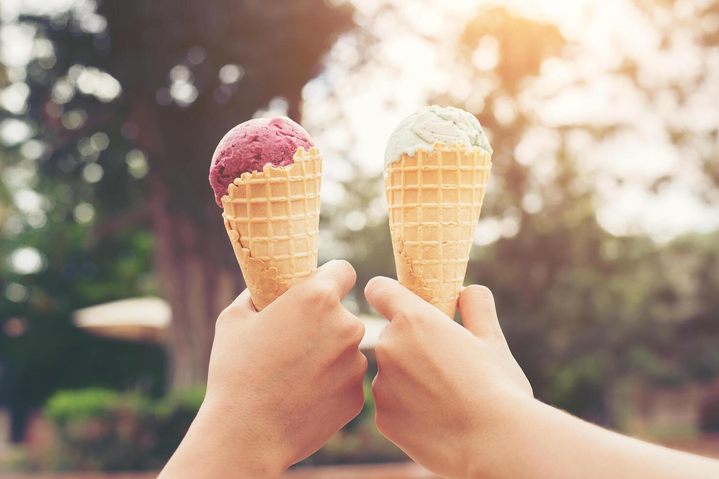 manos de mujer sosteniendo cono de gofre de helado derretido en las manos sobre fondo de naturaleza de luz de verano foto