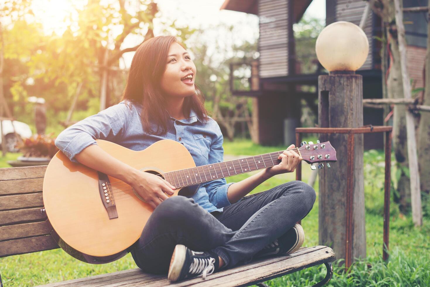 Beautiful young woman playing guitar sitting on bench, Happy time concept. photo