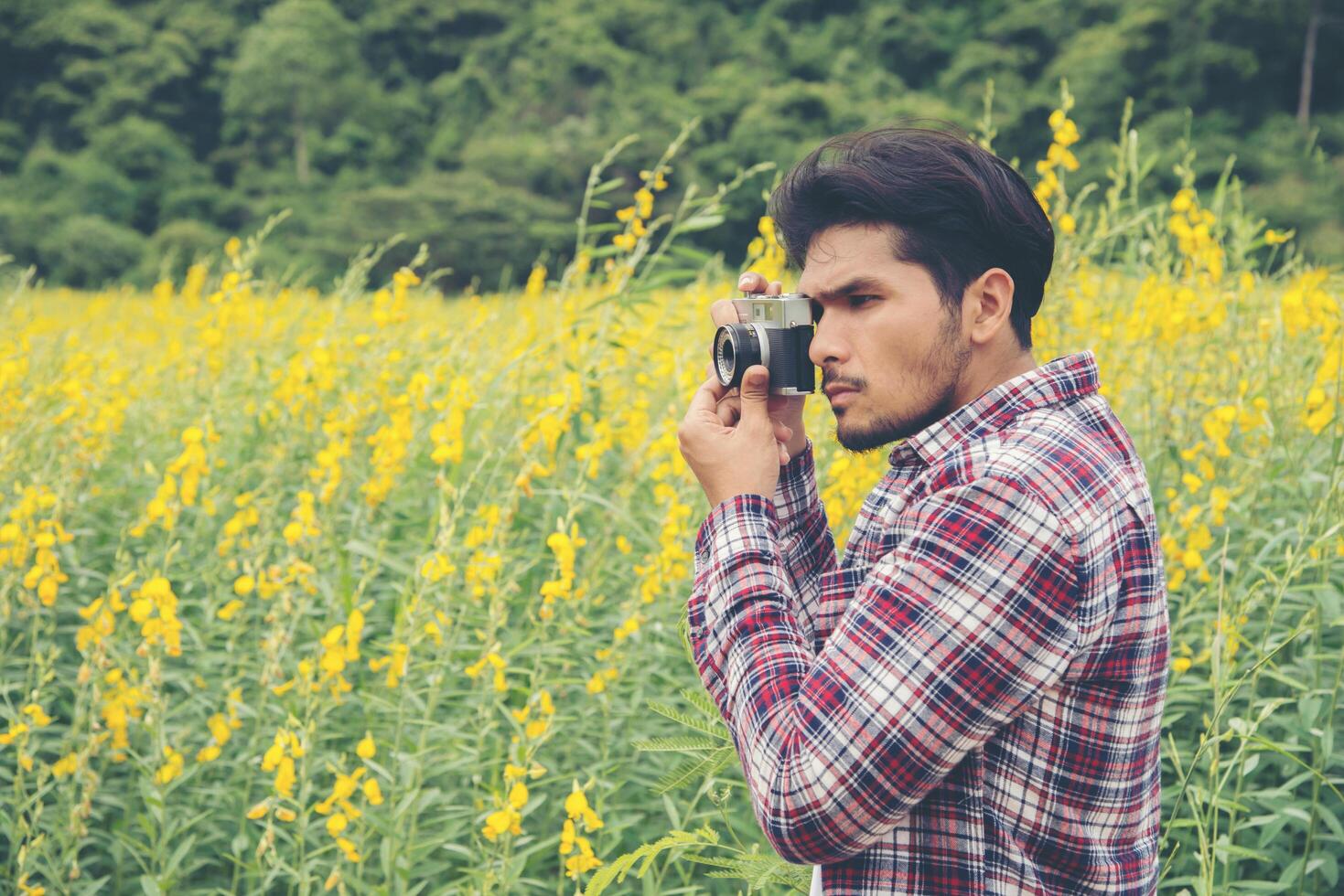 Young handsome hipster man photographing with retro camera with nature yellow flower field. photo